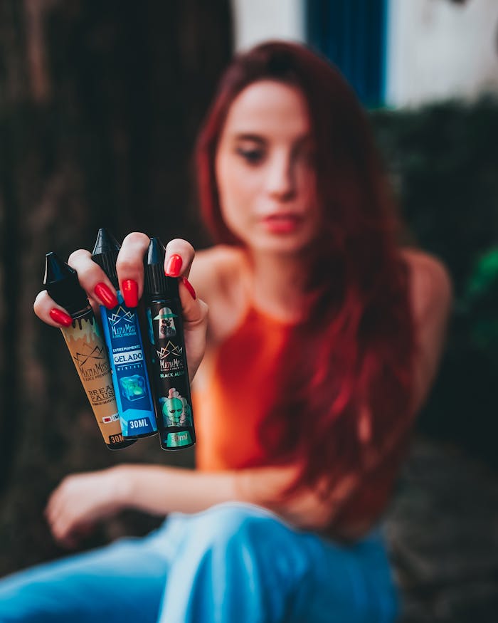 Woman with red nails showcasing three vape juice bottles in focus against a blurred background.